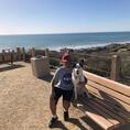 Adam sitting on a bench with dog, ocean background