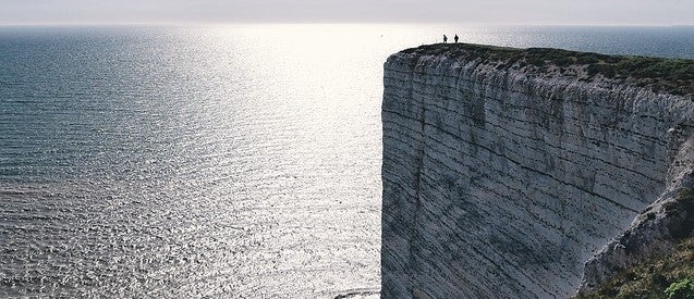 Two people standing on a huge rock formation overlooking the ocean